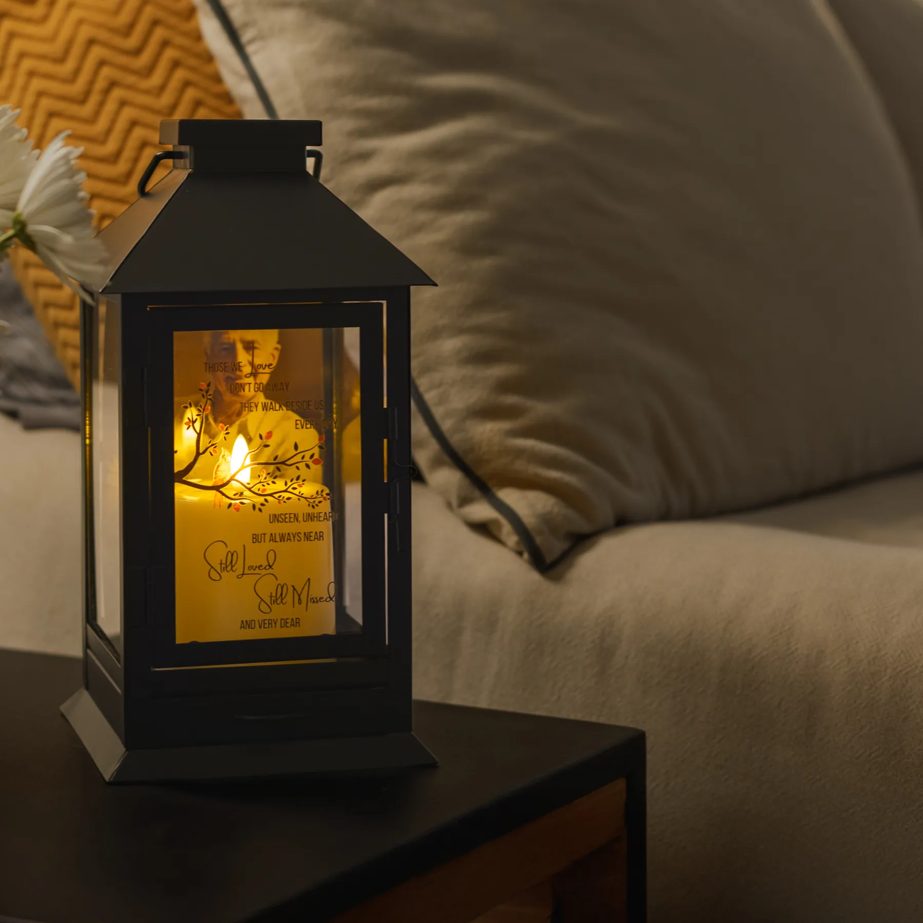 A black STILLWIND lantern lit on a side table, a photograph glowing behind the glass